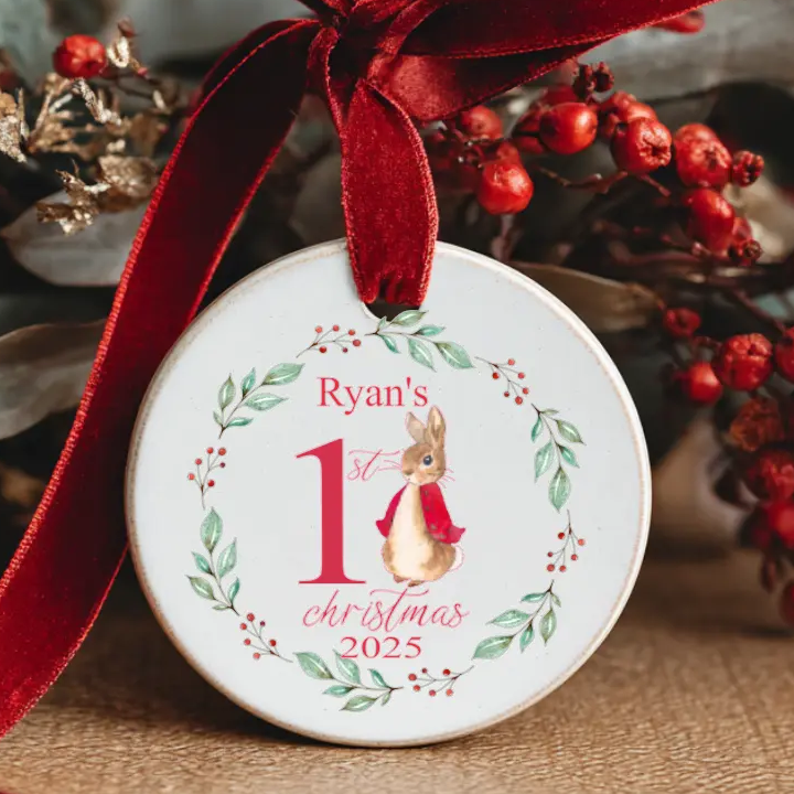 Personalised baby’s first Christmas 2025 ceramic ornament with woodland bunny design, festive holly wreath, and red velvet ribbon bow.