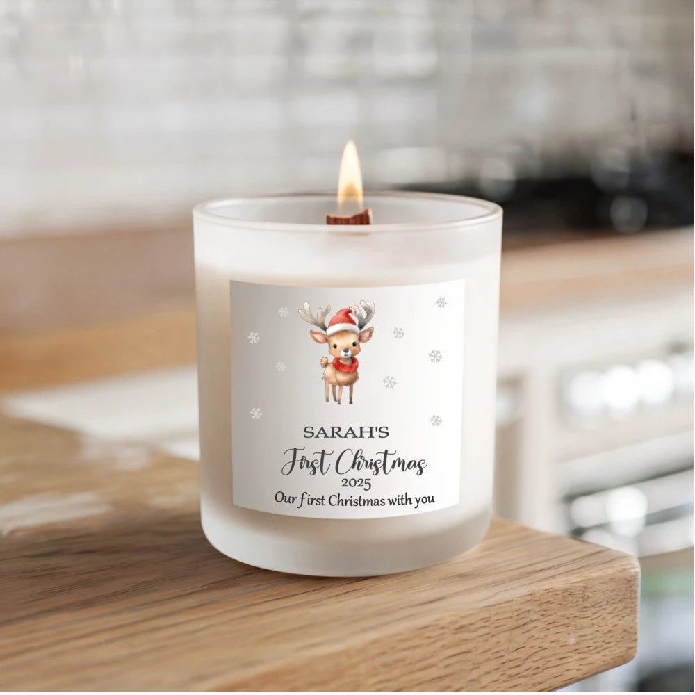 Hand‑poured soy candle with personalised label featuring a baby reindeer in a Santa hat and scarf, with the baby's name and First Christmas 2025