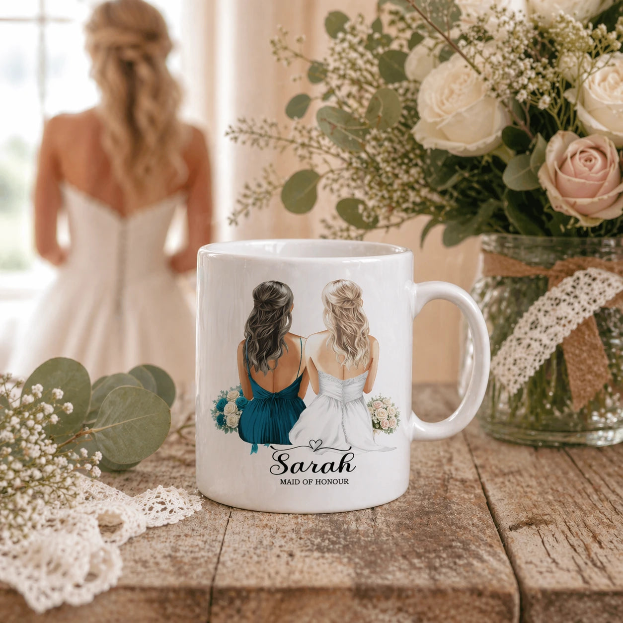 White personalised bridesmaid mug with bride and maid of honour illustration, placed on rustic wooden table with wedding flowers and bride in soft focus background