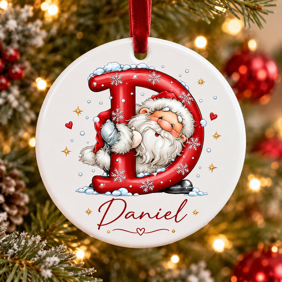 A personalized round Christmas ornament featuring a white background with a red hanging ribbon. The ornament is printed with a large red letter 'D' decorated with snowflakes and a smiling Santa Claus peeking behind it, with the name 'Daniel' written in red script at the bottom.