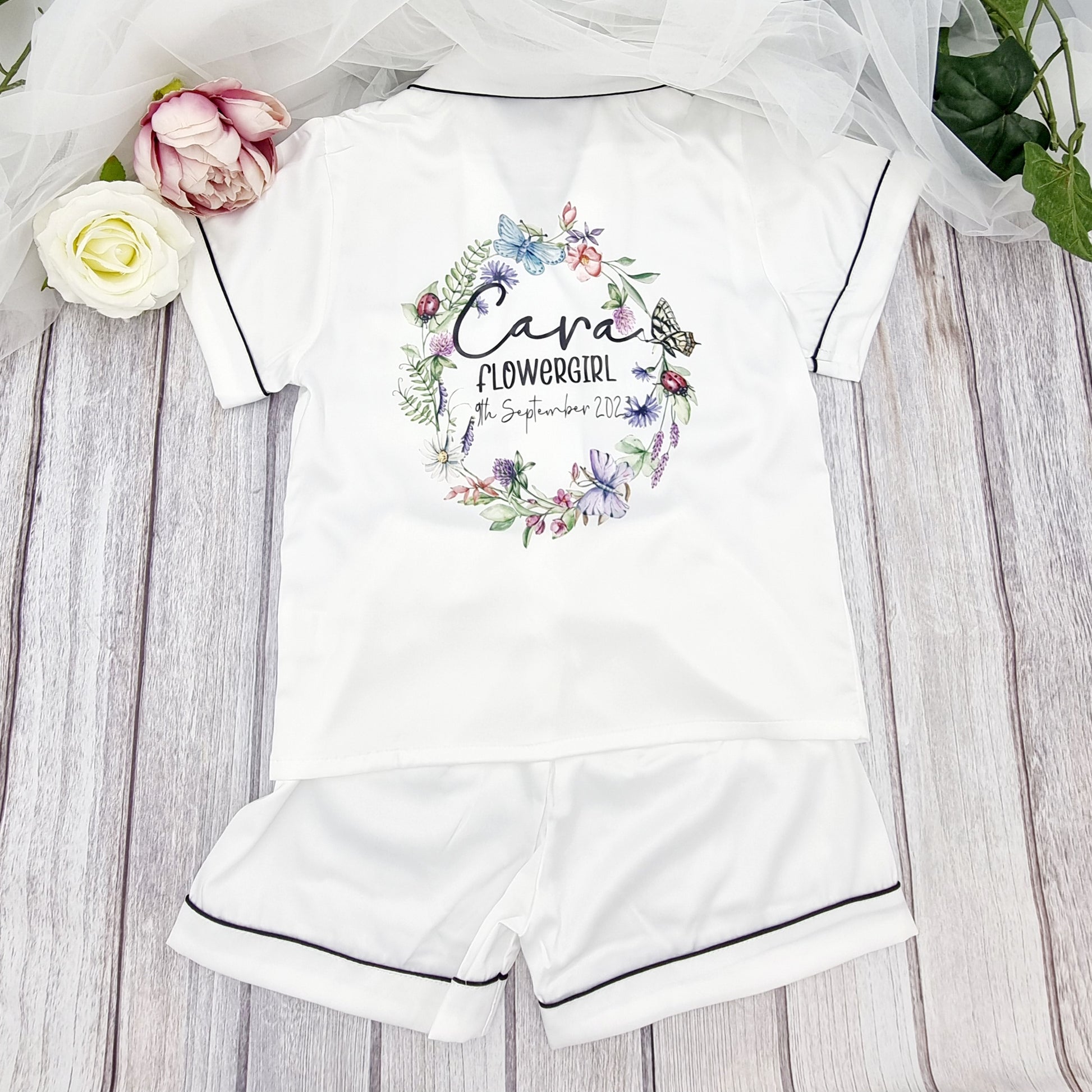 Personalised white satin flowergirl pyjamas with butterfly floral wreath design and custom name and wedding date, printed and finished in Ireland by HanaLee Studios.