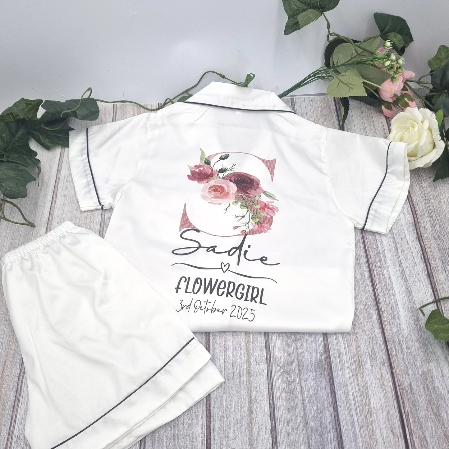 Personalised white satin flowergirl pyjamas featuring floral initial design with name and wedding date, printed and finished in Ireland by HanaLee Studios.