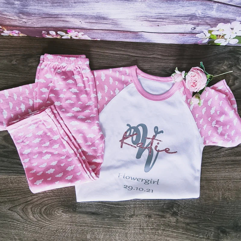 Personalised pink flower girl pyjamas with white cloud print and custom name and wedding date, printed and finished in Ireland by HanaLee Studios.