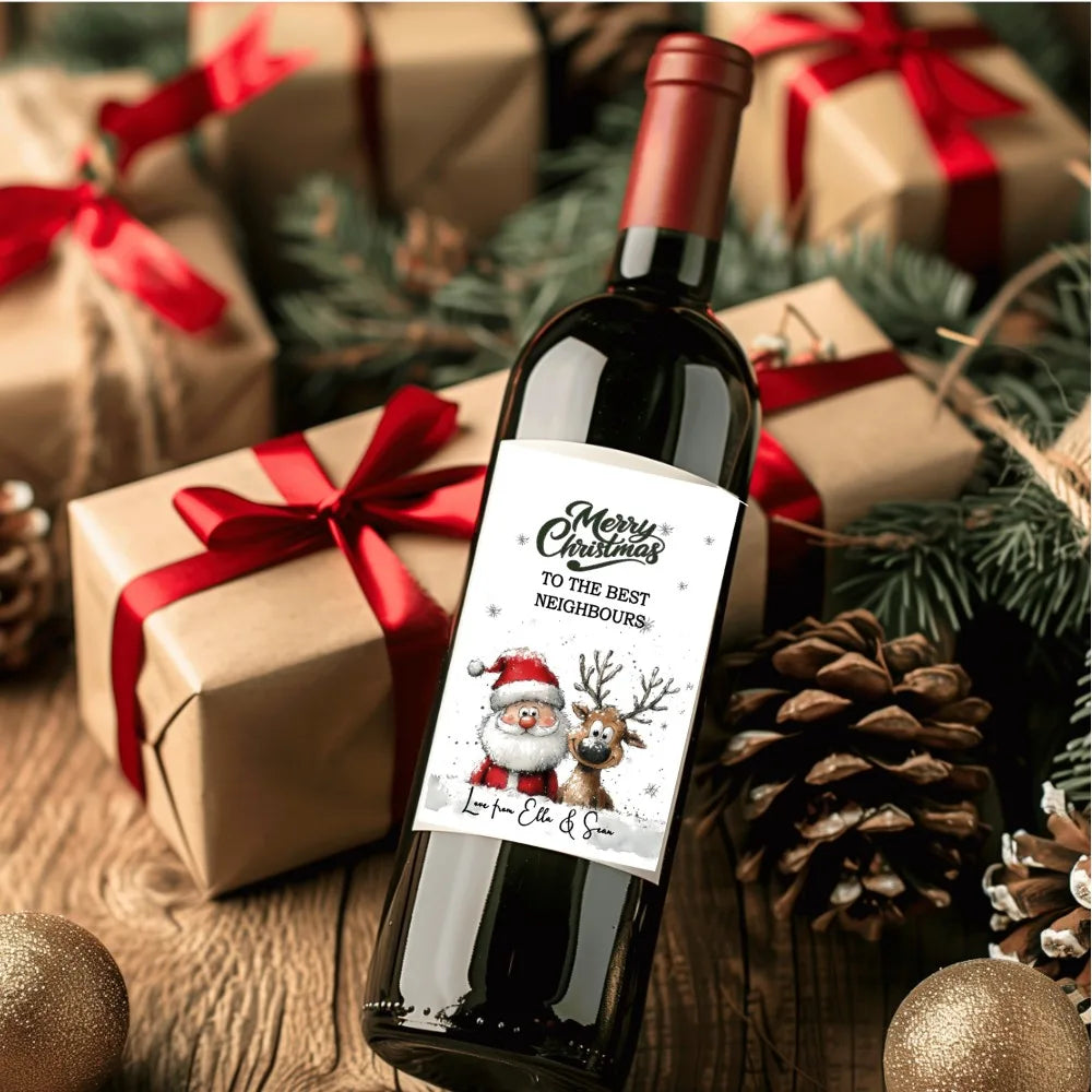 Personalised Santa and Reindeer Christmas wine bottle label with custom festive message, shown on a wine bottle surrounded by Christmas presents, pinecones, and decorations.