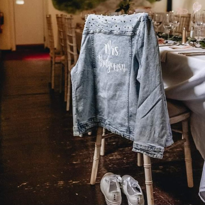 Denim jacket with 'Mrs. Bridgeman' on a chair at a wedding reception.