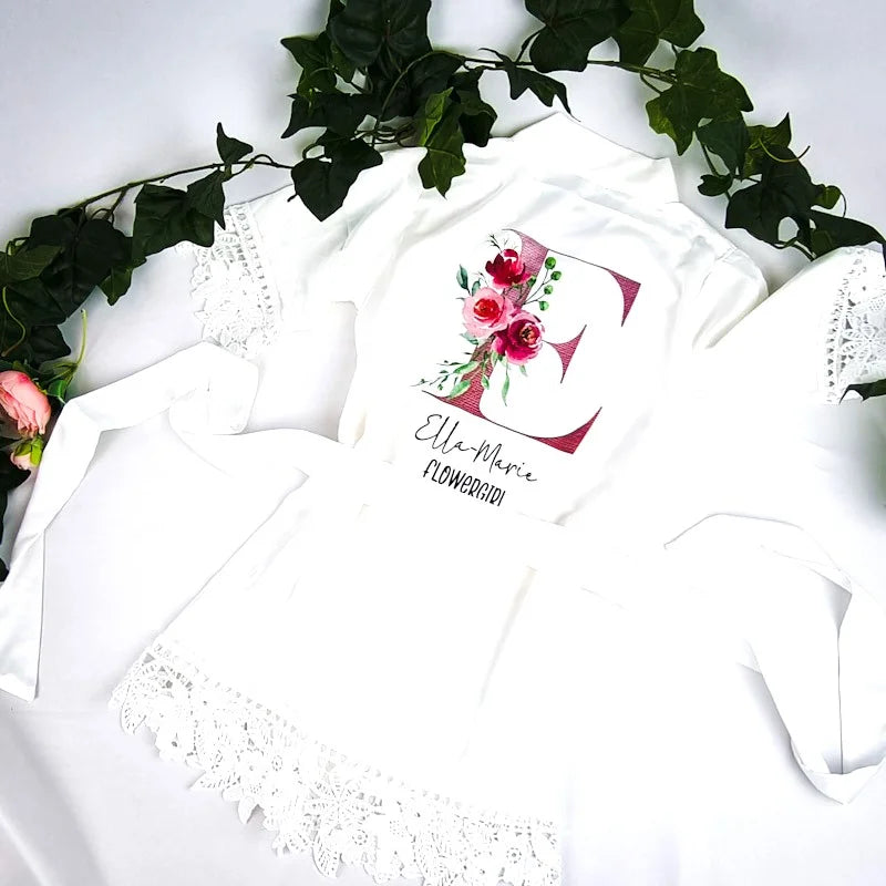 Personalised white satin flowergirl robe with lace trim and floral initial “E” design, customised with name and title, printed and finished in Ireland by HanaLee Studios.