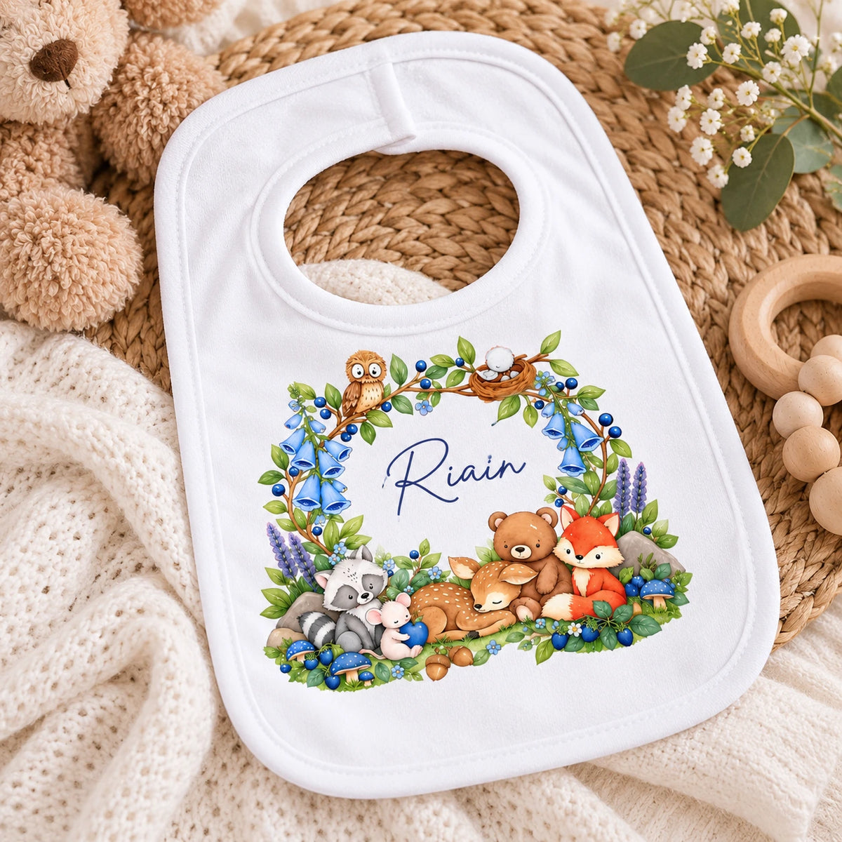 White personalised baby bib with name in blue lettering, woodland fox, deer, bear, owl, raccoon, mouse and blue floral design.