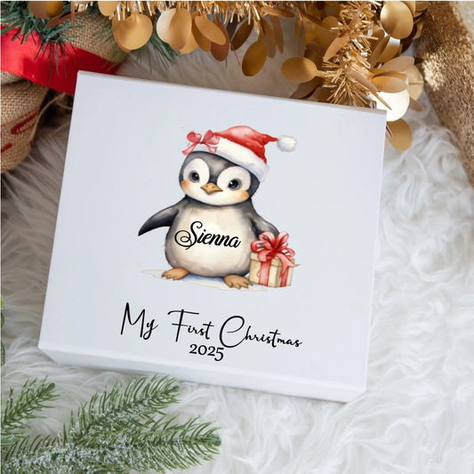 Illustrated personalised baby keepsake box showing a cute penguin wearing a Santa hat and holding a present. The penguin’s belly reads “Sienna,” and the box lid says “My First Christmas 2025”.