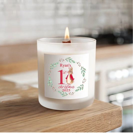 Hand‑poured soy candle in a frosted glass jar with wooden wick, featuring a personalised bunny wreath label that reads ‘Ryan’s 1st Christmas 2025