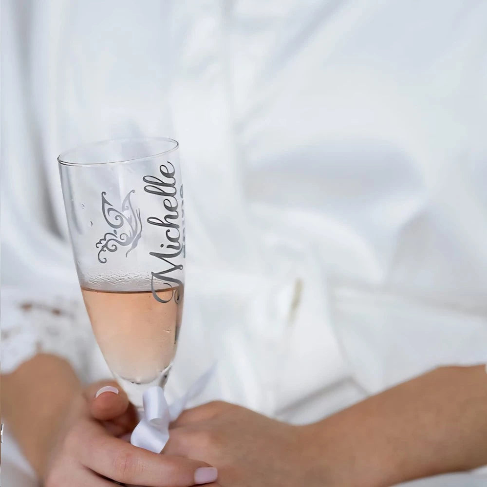 Bride in her white robe holding a champagne flute personalised with her name. 