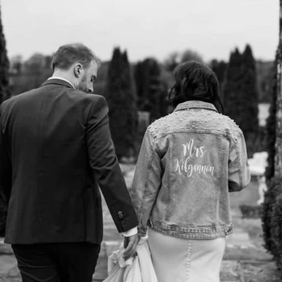 Bride and her husband on their wedding day. The bride is wearing her personalised bridal denim jacket with her new name on the back. 