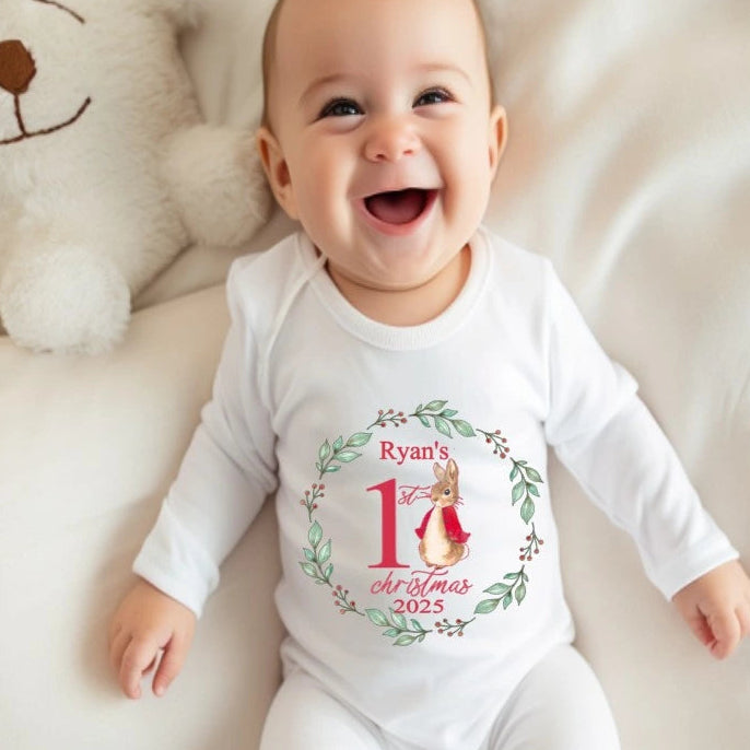 A baby in a white babygro printed with a cute rabbit wreath design personalised with baby's name and first christmas 2025 