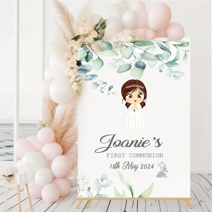 A3-sized personalized first communion sign featuring a cartoon illustration of a girl, name Joanie, with floral decorations and the date of the first communion, displayed on a wooden easel.