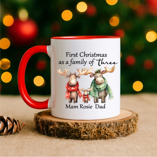 Personalised Christmas mug with red handle reading “First Christmas as a Family of Three” with moose family illustration – custom Irish gift for new parents.