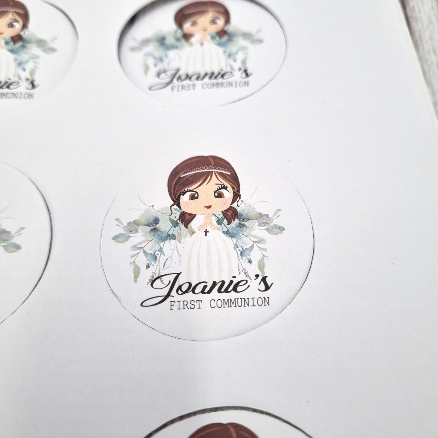 Close up view of First Communion sticker sheets with floral wreaths and script text, personalised name and date stickers