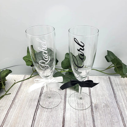 Pair of custom wedding champagne glasses with bride and groom names in black and white vinyl.