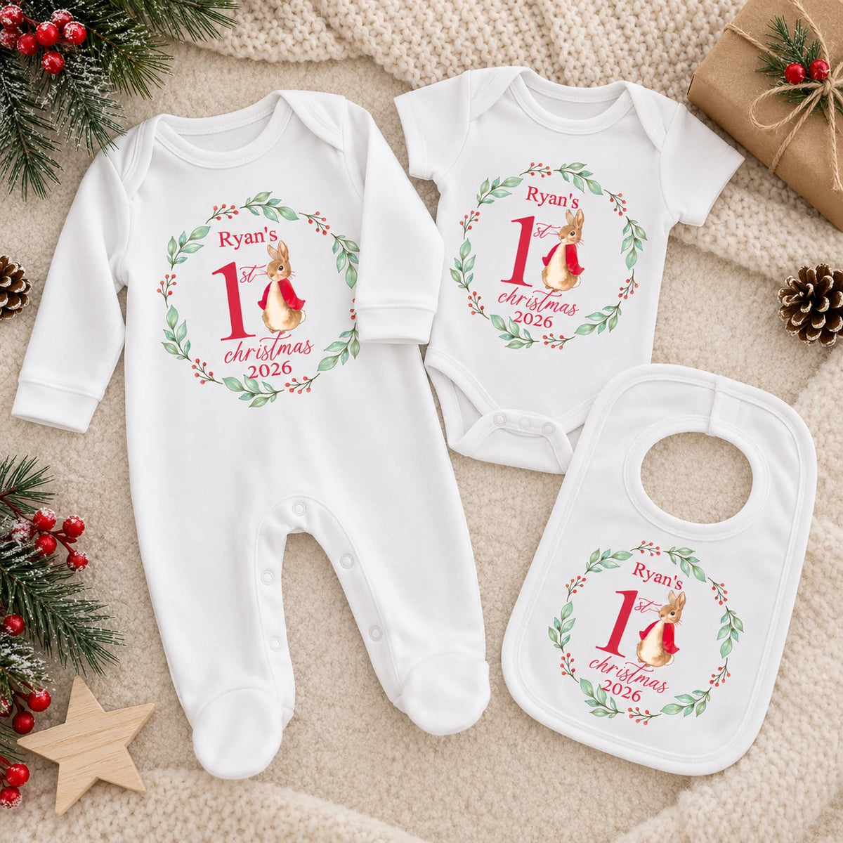 Personalised Baby's First Christmas outfit bundle featuring a white babygro, vest and bib with matching bunny, holly wreath and 2026 design, laid out on a neutral Christmas background.