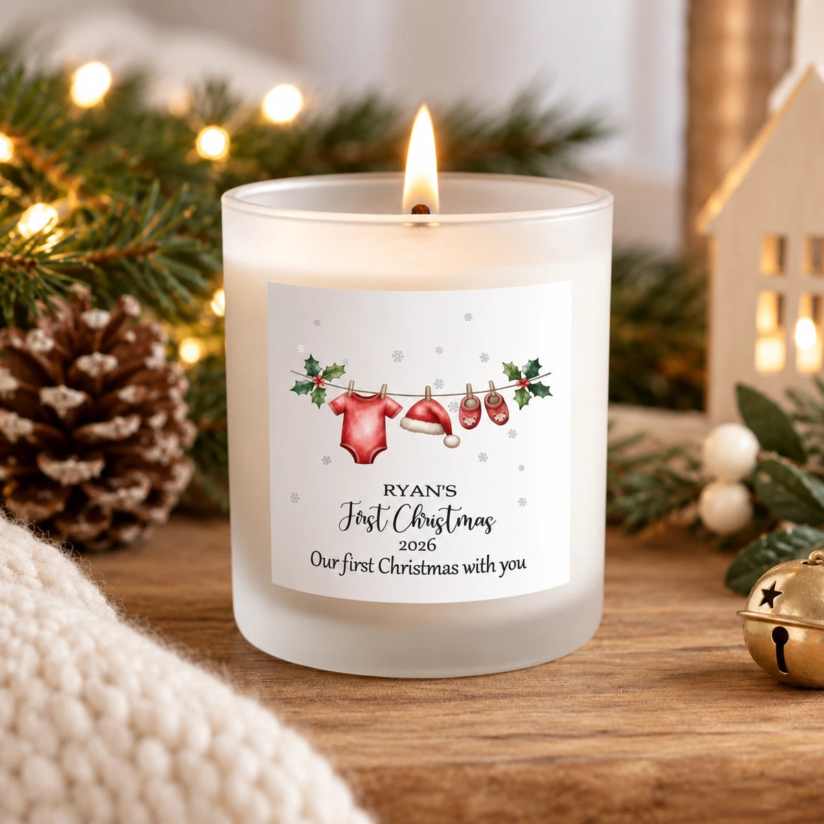 Personalised Baby's First Christmas 2026 soy wax candle in a frosted white glass jar, featuring the name and a Christmas baby clothesline design, displayed in a cosy Christmas setting.
