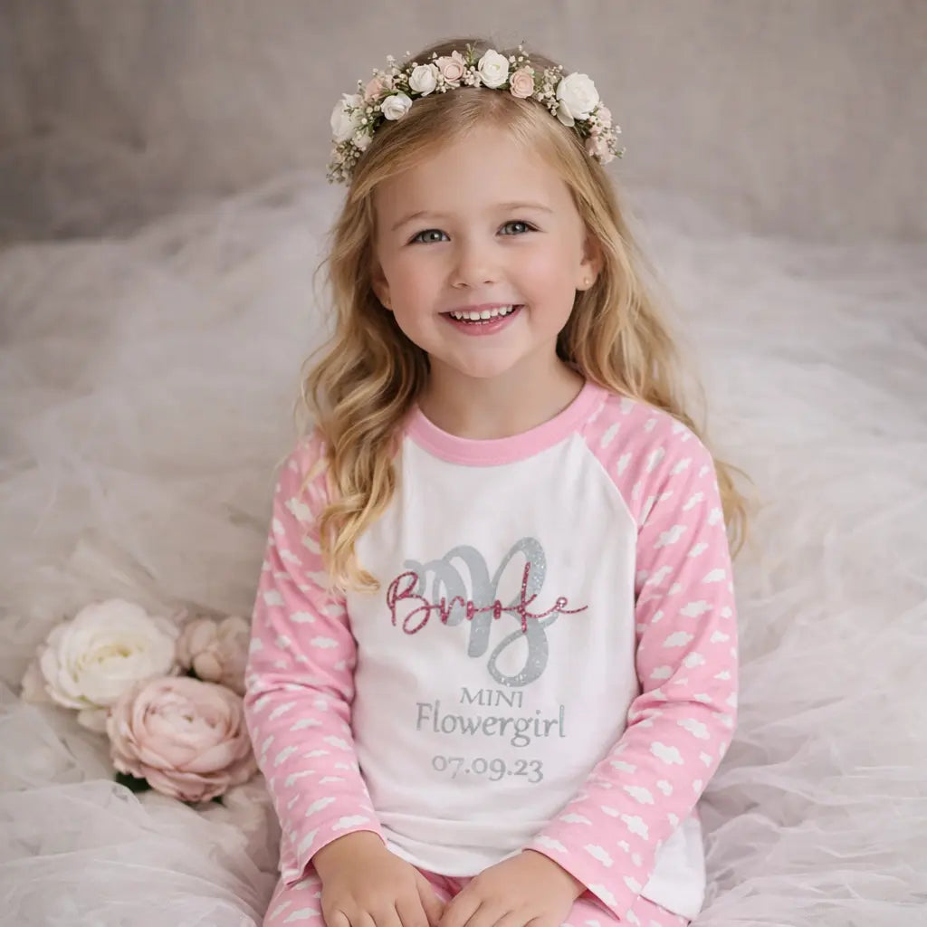 Flower girl wearing personalised pink cloud pyjamas with name and date, sitting on soft tulle with floral crown, perfect for wedding morning getting ready in Ireland