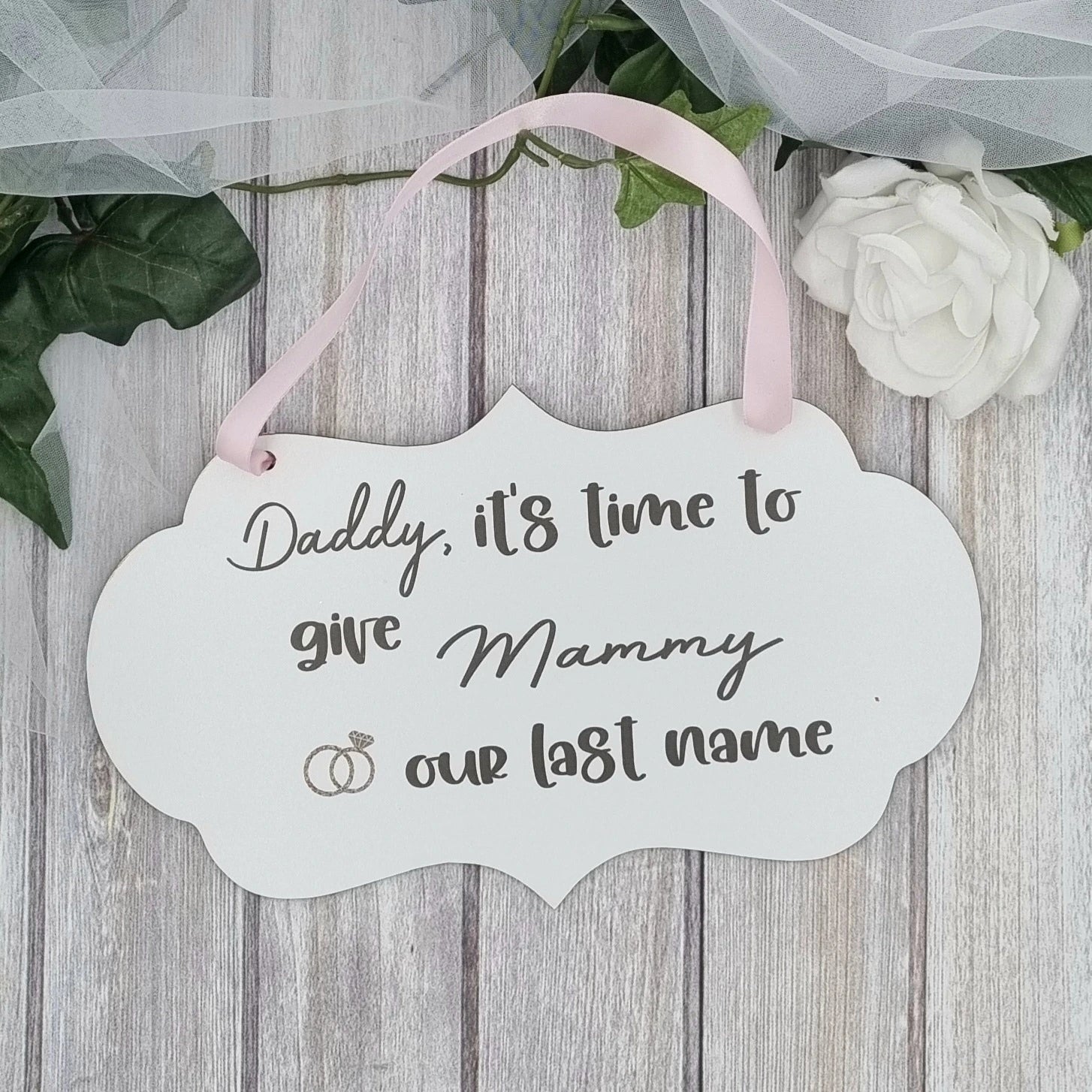 Flower girl wedding sign with pink ribbon reading “Daddy, it's time to give Mammy our last name”
