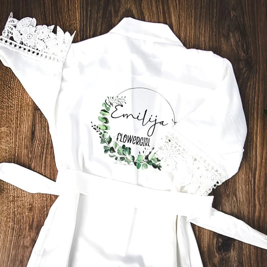Personalised white satin flowergirl robe with lace trim and eucalyptus design, customised with name ‘Emilija’ — designed and finished in Ireland by HanaLee Studios.