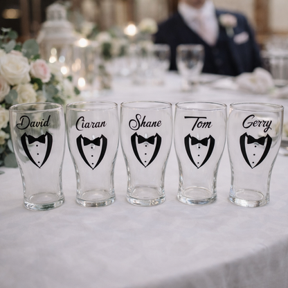 Personalised groomsmen pint glasses with tuxedo design and names displayed on a wedding table setting, ideal gift for best man and groomsmen in Ireland
