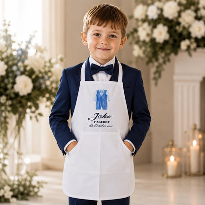 Young page boy wearing a navy suit and a personalised white wedding apron with his name and wedding date, protecting his clothes while helping with wedding day preparations.