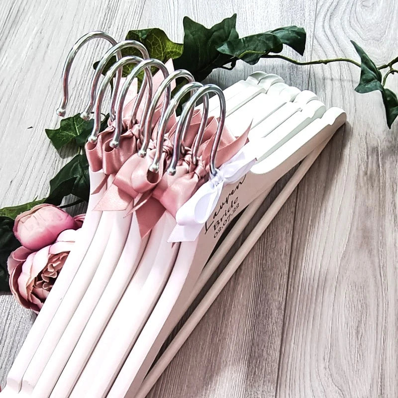 Personalised wedding hangers with pink ribbon for bride and bridesmaids displayed together on wooden background