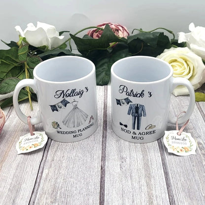 Two matching personalised wedding planning mugs displayed with floral props, showing bride and groom illustrations, handmade by HanaLee Studios.