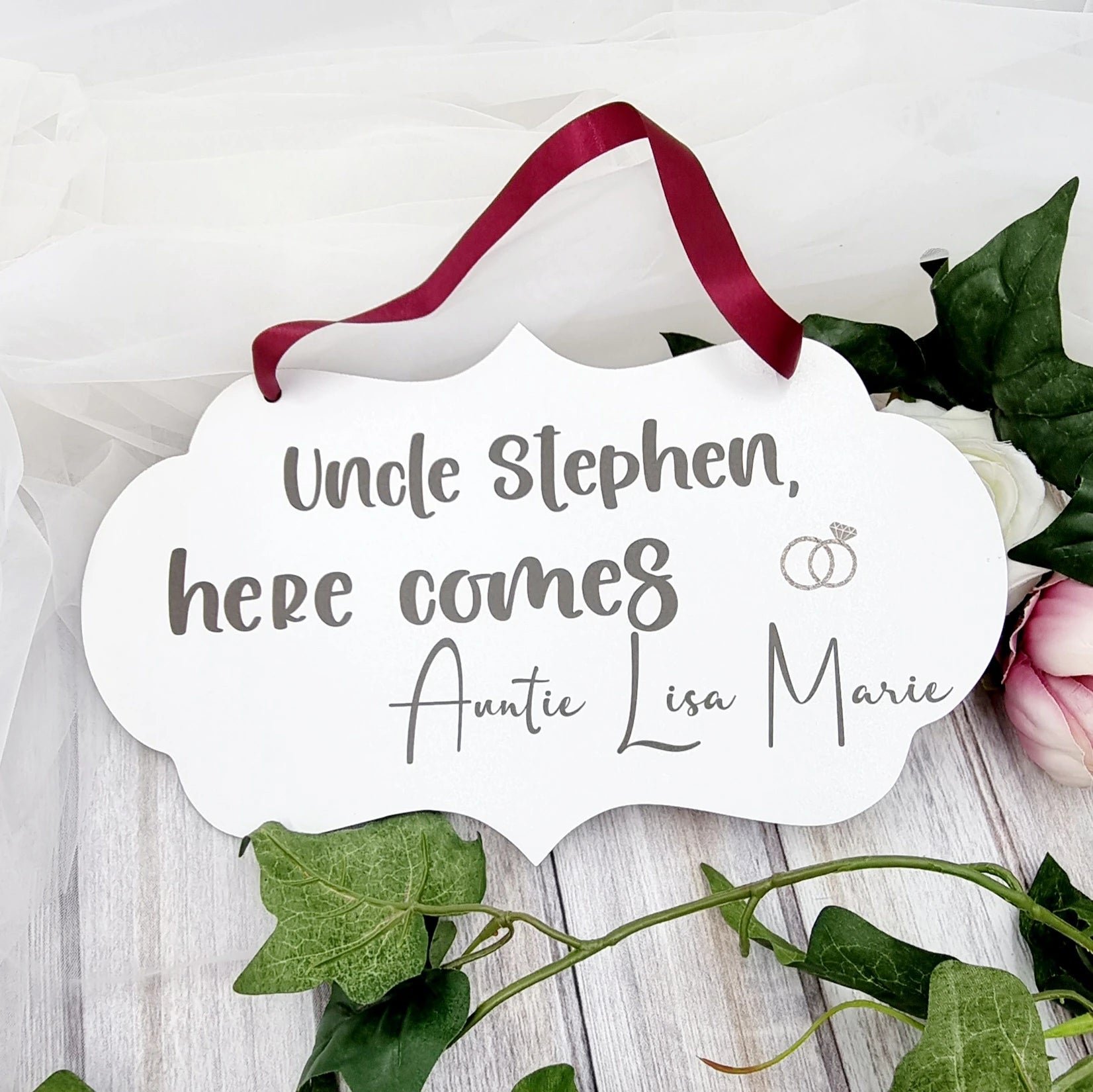 Personalised flower girl wedding sign with red ribbon reading “Uncle Stephen, here comes Auntie Lisa Marie”
