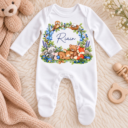 White personalised baby sleepsuit with name Riain, blue woodland flowers and illustrations of a fox, deer, bear, owl, raccoon and mouse.