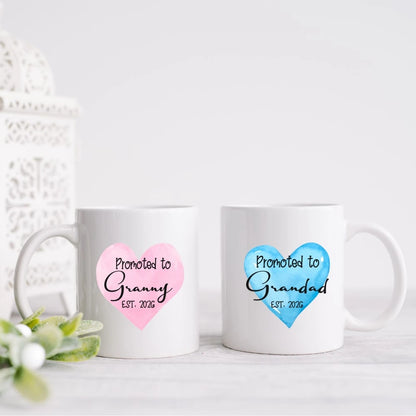 White ceramic mugs with pink and blue heart designs reading Promoted to Granny and Promoted to Grandad, personalised pregnancy announcement gift handmade in Ireland.