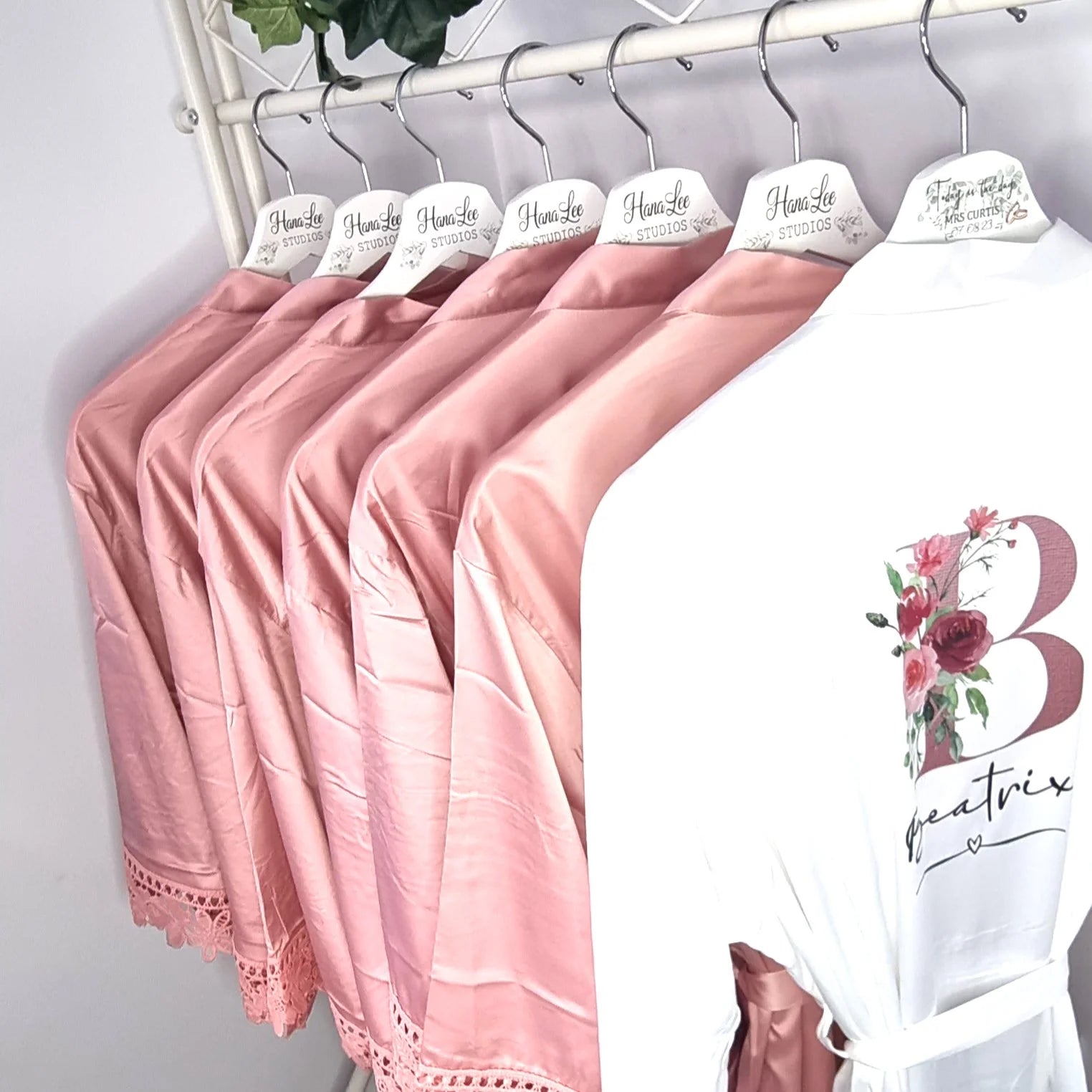 Row of blush pink bridesmaid robes with white bride robe featuring floral initial design – printed in Co. Meath, Ireland.