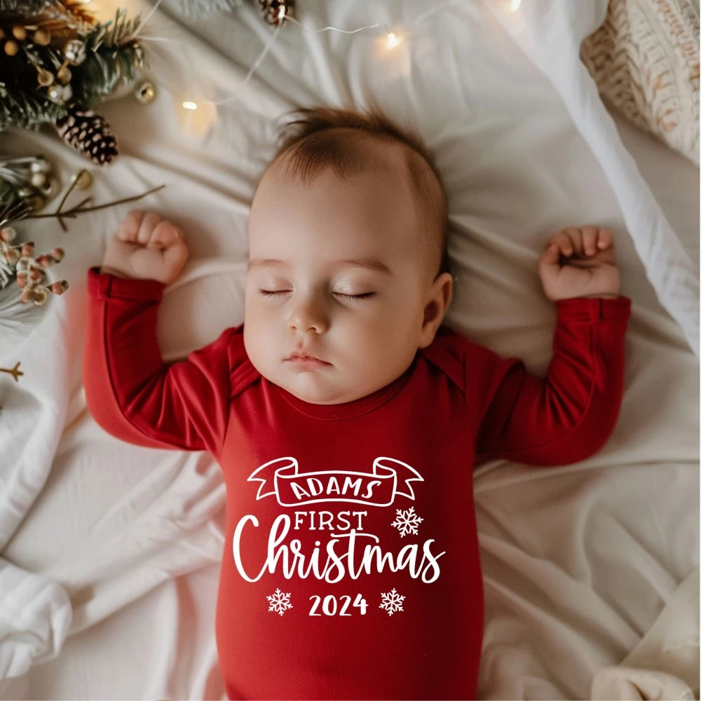 Baby asleep wearing a red personalised babygro with Baby's first Christmas written on the front. 