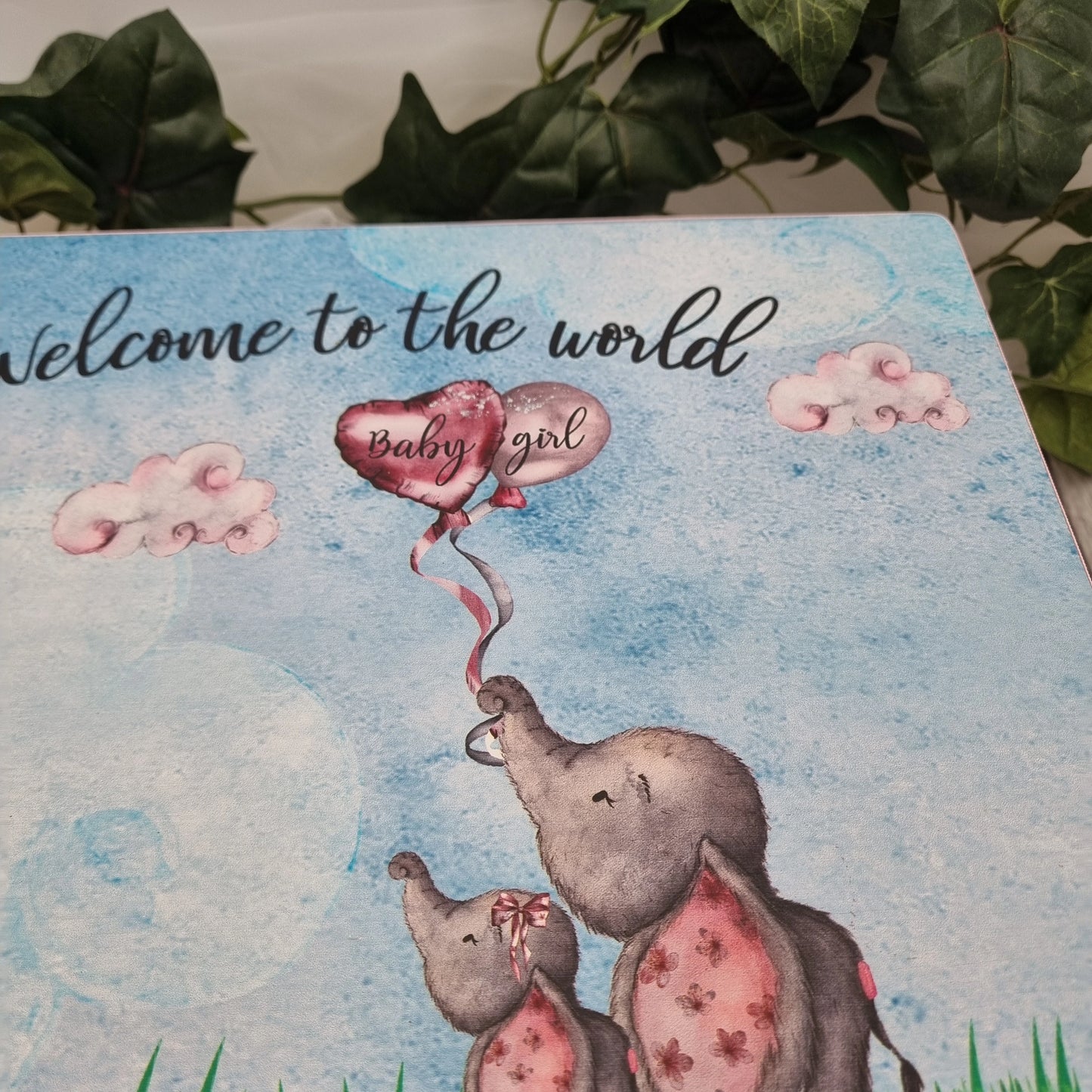 Close up of personalised baby elephant keepsake box lid featuring welcome to the world design and heart balloon, available for baby boy or baby girl with blue or pink ribbon, Irish made gift.