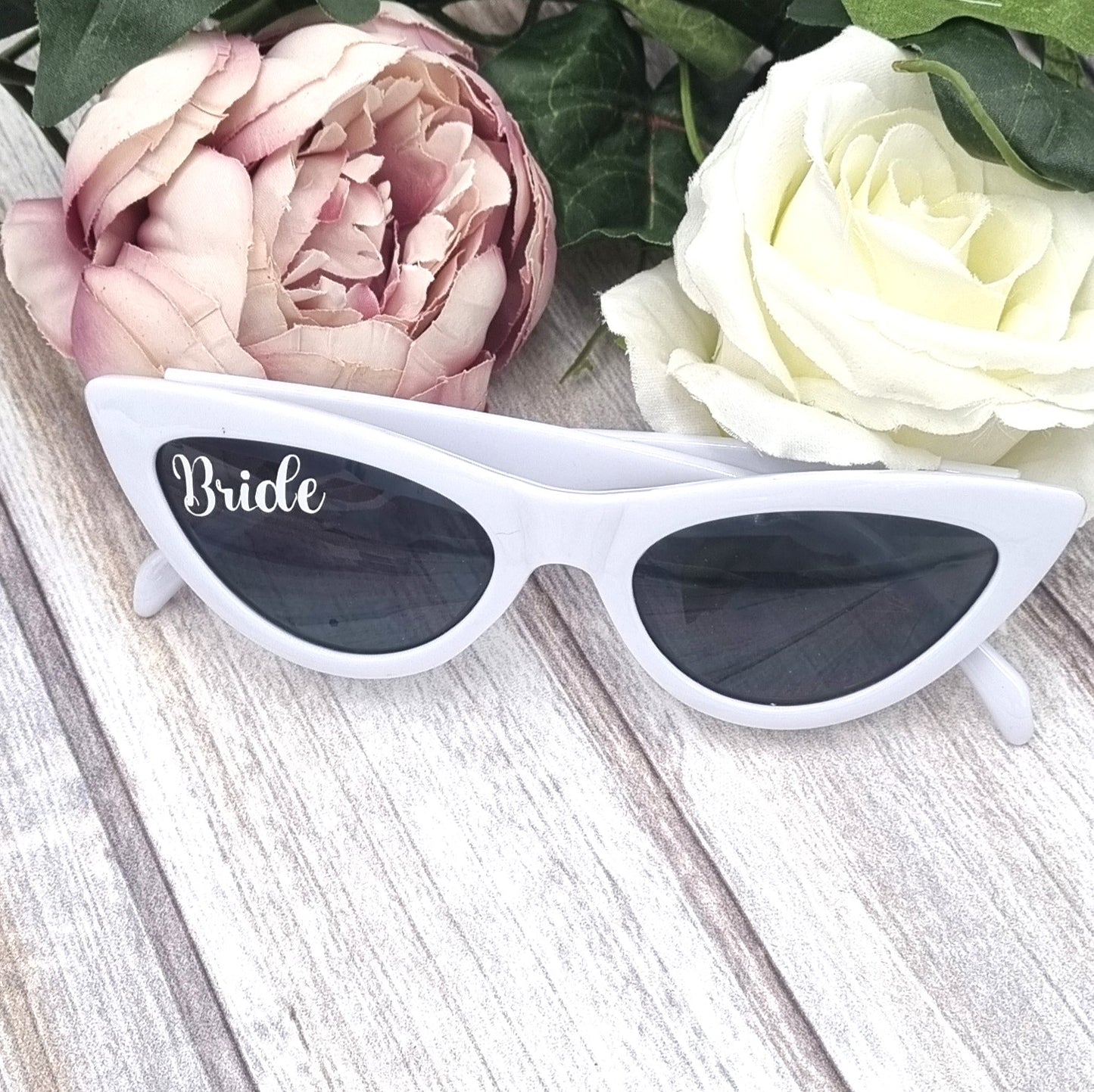 White sunglasses with black lenses and Bride text on one lense. 